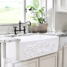 a white kitchen sink sitting under a window next to a potted plant on top of a counter