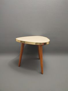 an oval table with wooden legs and a white top on a gray background in front of a grey wall