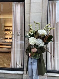 a woman standing in front of a store holding a vase with flowers on the outside