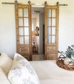 a bed with white sheets and pillows in front of two wooden doors that lead to another room