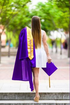 a woman in a graduation gown walking down the street with her purple and gold stole