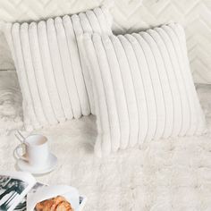 two white pillows sitting on top of a bed next to a cup and saucer