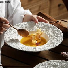 a person holding a wooden spoon over a bowl of food on a white plate with crumbs