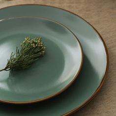 two plates with green and gold rims on top of each other, one has a sprig of rosemary