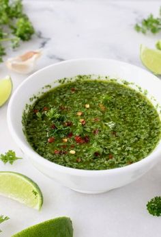 a white bowl filled with green salsa next to limes