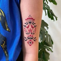 a woman's arm with a red and black flower tattoo on the left forearm