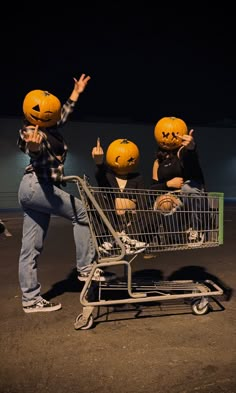 three people in pumpkin heads sitting on top of a shopping cart with their hands up