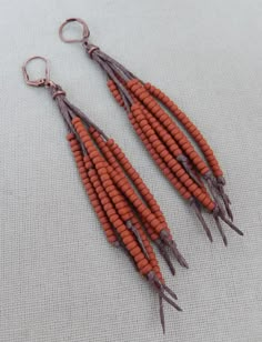 two pairs of orange beads hanging from hooks on a white cloth covered surface with silver earwires