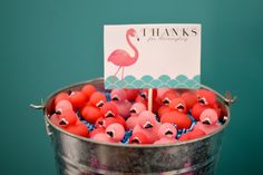 a bucket filled with pink flamingos sitting on top of a wooden table next to a sign