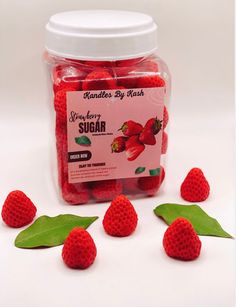 a jar filled with red raspberries next to green leaves