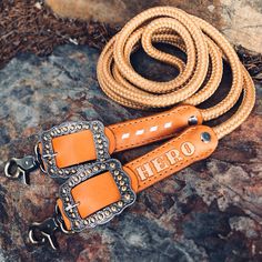 a pair of leather reins sitting on top of a rock next to an orange rope