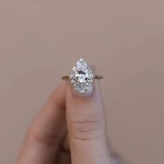 a woman's hand holding an engagement ring with a pear shaped diamond