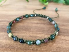 a bracelet with beads and stones on a wooden table next to plants, leaves and flowers