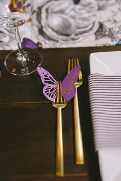 a close up of a table with gold utensils and purple butterfly napkins