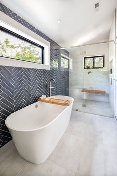 A large garden tub for soaking beneath a high window. In the back, a large zero-entry shower with glass divider and a bench. Rear wall is blue herringbone tile. Accent Wall Bathtub, Free Standing Tub Accent Wall, Tile Wall Behind Free Standing Tub, Accent Wall Behind Bathtub, Tub Accent Wall, Tile Behind Tub, Zero Entry Shower Master Bath, Zero Entry Shower Ideas, Herringbone Shower Wall