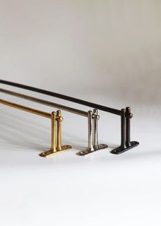 three metal and brass railings are lined up against a white background, one is black the other is gold