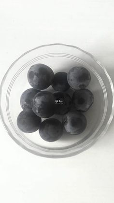 a glass bowl filled with black plums on top of a white countertop next to a knife and fork