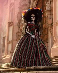 a skeleton in a mexican dress and sombrero stands on the steps outside an old building