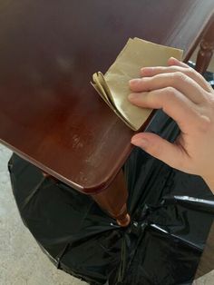 a person holding onto a piece of brown paper on top of a wooden table with black plastic covering it