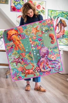 a woman is holding up a colorful quilt