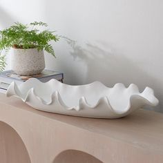 a white bowl sitting on top of a wooden table next to a potted plant