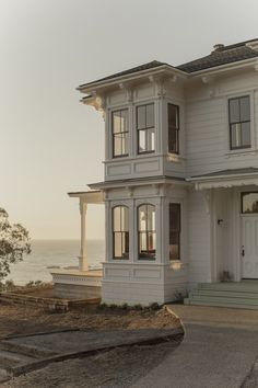 a large white house sitting on the side of a road next to the ocean in front of it