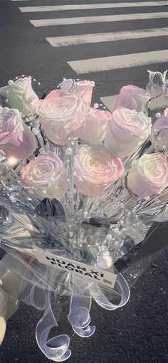 a clear vase filled with pink roses on top of a parking lot next to a crosswalk