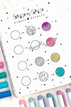 an open notebook with some markers and pens on it next to the pages that have planets drawn