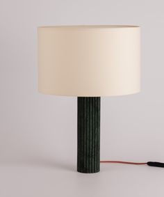 a lamp with a white shade on it and a black cord connected to the base