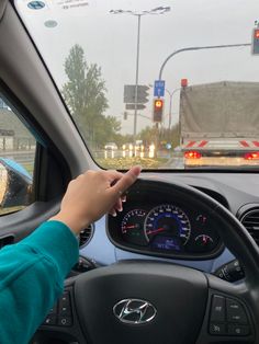 a person driving a car in the rain with their hand on the steering wheel and dashboard