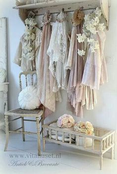 there are many dresses hanging up on the wall next to a bench and table with flowers