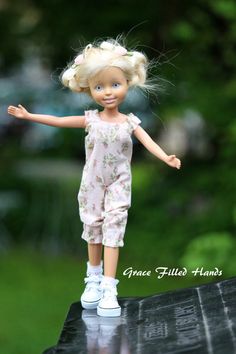 a doll with blonde hair is standing on a black surface and has her arms outstretched