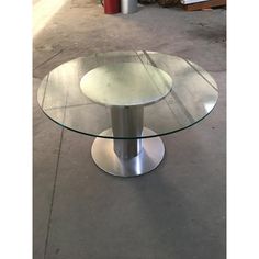 a round glass table with metal base on concrete floor next to fire hydrant and trash can