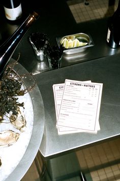 there is a menu on the table next to some wine bottles and oysters in bowls