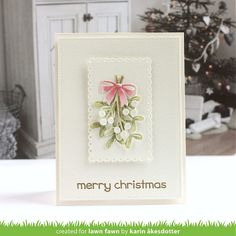 a christmas card with a pink bow and holly on the front, sitting on top of a table