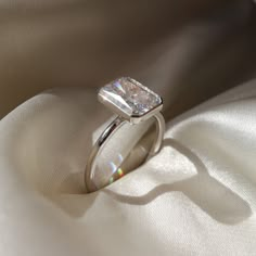 a diamond ring sitting on top of a white satin covered cloth with the light shining through it