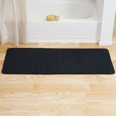 a black bath mat sitting on top of a wooden floor next to a white tub