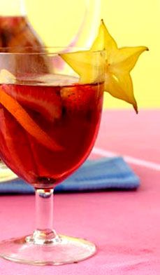 a glass filled with liquid sitting on top of a pink table covered in fruit and veggies