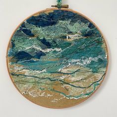 an embroidered wall hanging with blue and green watercolors on the outside, in front of a white wall