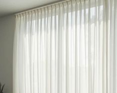 a window with white sheer curtains and a potted plant