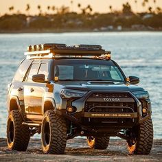 the toyota truck is parked on the beach by the water with its lights turned on