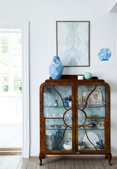 a wooden cabinet with glass doors in a living room next to a painting on the wall