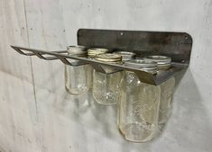 four mason jars are hanging from a metal shelf on the wall, and one is empty