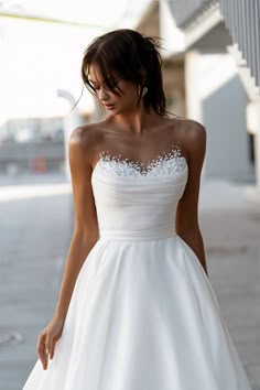 a woman in a white wedding dress is walking down the street with her hand on her hip