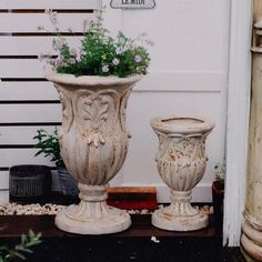 two white vases with flowers in them sitting next to each other on the ground