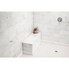 a white tiled shower with two statues on the bench next to it and a hand held shower head in the corner