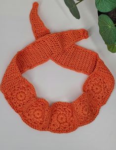 an orange crocheted scarf next to a potted plant