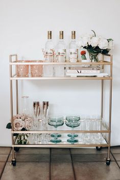 a gold bar cart with glasses and bottles on the top, flowers in vases next to it