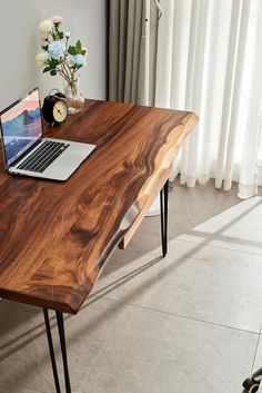 a laptop computer sitting on top of a wooden desk next to a vase with flowers