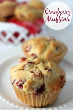 two cranberry muffins on a white plate next to another muffin